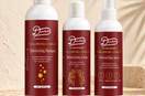 Daurham Calling All Curls Moisturizing Shampoo, Moisturizing Lotion and Moisturizing Spray in white bottles with deep red labels on a travertine stone ledge